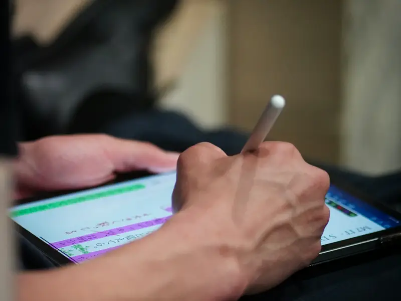 A hand writing on a tablet screen with a stylus.