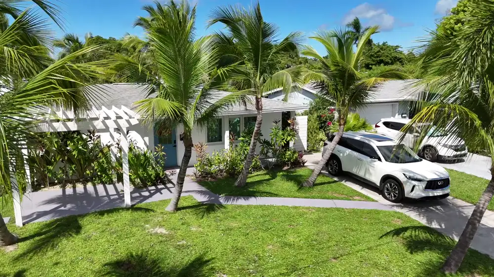 A single-storey rental house behind palm trees, seen from the street.