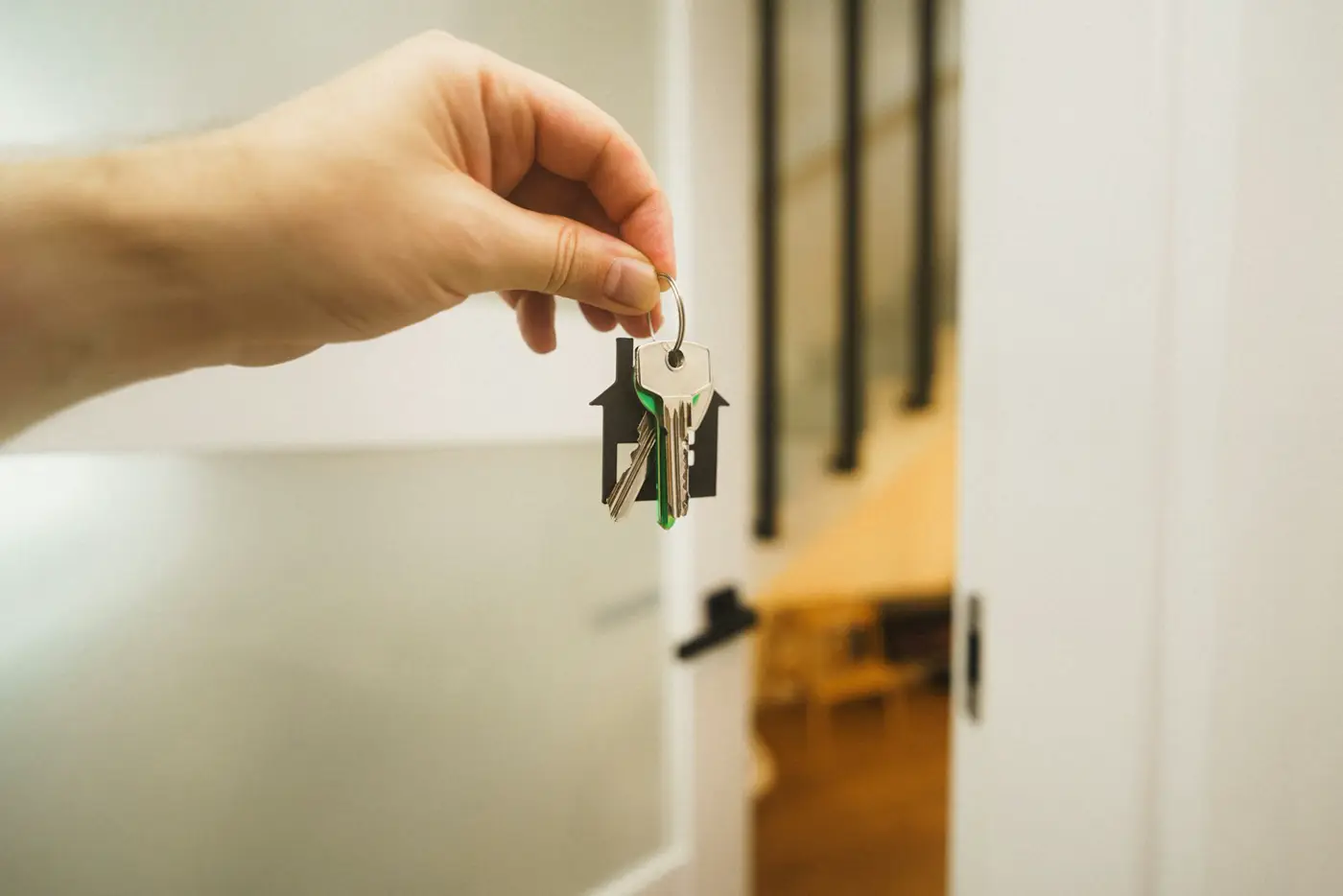 A hand holding up a set of house keys on a house-shaped key ring.