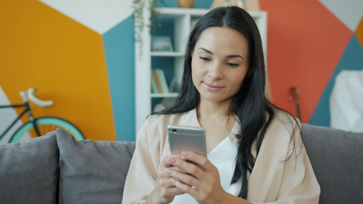 A woman on a sofa smiling at her phone.